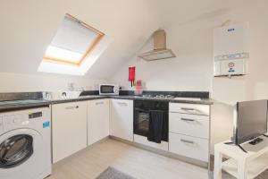 a kitchen with white cabinets and a washer and dryer at Crosshills Serviced Apartments in Leeds