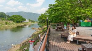 a woman holding a dog sitting on a bench next to a river at Gapeong Jason Spa Pension in Gapyeong