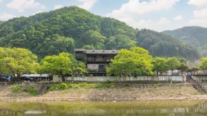 a building next to a river with a mountain at Gapeong Jason Spa Pension in Gapyeong