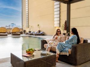 two women sitting on chairs next to a pool at Ibis Jeddah Malik Road in Jeddah
