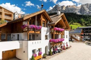 a building with flowers on the balconies with mountains in the background at Hotel Vajolet in San Cassiano
