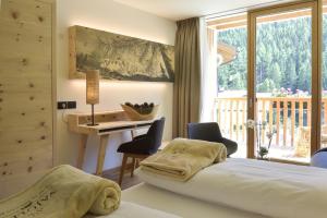 a bedroom with a bed and a desk and a balcony at Hotel Vajolet in San Cassiano