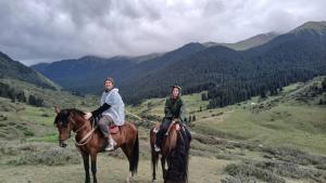 two people riding on horses in a mountain valley at Yurt On The Mountain -With us you will feel the spirit of nomads in Svetlaya Polyana