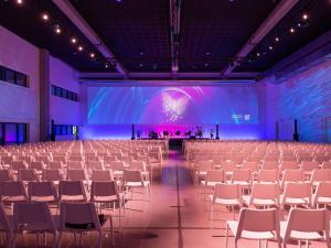 an empty banquet hall with white chairs and a stage at ibis Styles Namur in Namur