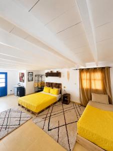 two beds in a room with yellow sheets and a rug at Yousurf Surf House in Essaouira