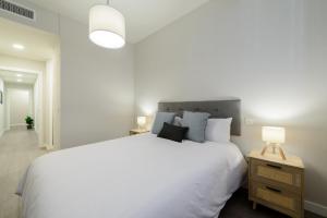 a white bedroom with a large bed and a lamp at Torrejón Suites in Torrejón de Ardoz