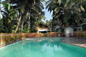 a swimming pool in front of a fence with palm trees at Betel Leaf Resort in Māhīm +3 photos