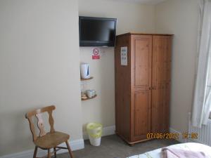a room with a chair and a tv and a cabinet at Sefton Lodge SEAFRONT ,PANORAMIC SEA VIEW ENSUITE BALCONY ROOMS AVAILABLE, GUEST GARDEN in Paignton