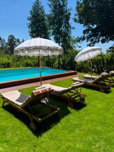 two lounge chairs and umbrellas next to a swimming pool at Casa da Costeira in Figueiró
