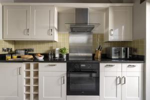 a kitchen with white cabinets and a black oven at Perry Cottage in Halford +17 photos