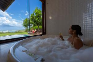 a woman sitting in a bath tub with a glass of wine at Gungaporanga Hotel in Barra de São Miguel