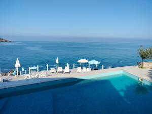 a swimming pool with chairs and umbrellas and the ocean at Apartments Harmony in Utjeha