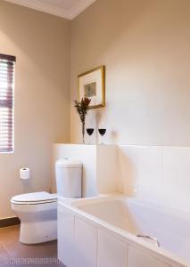 a bathroom with a tub and a toilet and two glasses of wine at Pond End Villa in Clarens