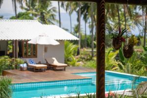 a resort with a swimming pool with chairs and an umbrella at Hygge Residence - Barra Grande - Península de Maraú in Marau