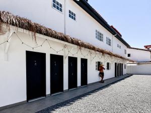 a woman walking past a white building with black doors at Raya Beach Studios in Maresias