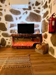 a living room with a fireplace with a tv on a stone wall at Refúgio d’Aldeia da Serra in Seia