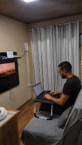 a man sitting on a couch with a laptop computer at Chalé Romântico Privativo com Lareira e vista para Montanhas in Capela do Alto