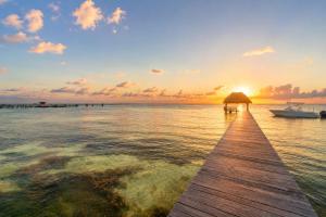 a pier with a boat on the water at sunset at Sunset Condo 104 Puerta al Mar Isla Mujeres Mexico in Isla Mujeres