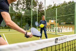 a woman holding a tennis racket and a ball on a court at Landal Namur Nature in Gesves