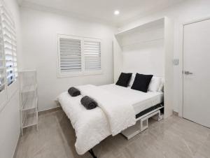 a white bedroom with a white bed with black pillows at Cara Luxe Stays at Regents Park near Olympic Park and DFO in Regents Park