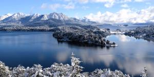 an island in the middle of a lake with snow covered mountains at Pacha Home By A.M.A in San Carlos de Bariloche