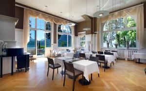 a restaurant with white tables and chairs and large windows at Parkhotel Gunten – Beach & Spa in Gunten