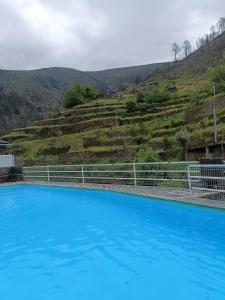 a blue swimming pool with a hill in the background at Refúgio do Xekeraute in Piódão