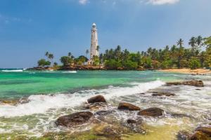 a lighthouse on a beach with rocks in the water at Monaco Guest House in Devinuwara
