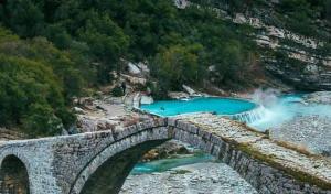 a stone bridge over a river with blue water at Guesthouse - VILA QETESIA in Përmet