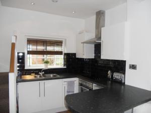 cocina con armarios blancos y encimera negra en Yarm View Cottages, en Yarm