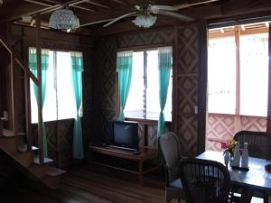 a dining room with a table and a tv and windows at Mayas Native Garden Resort in Basdiot