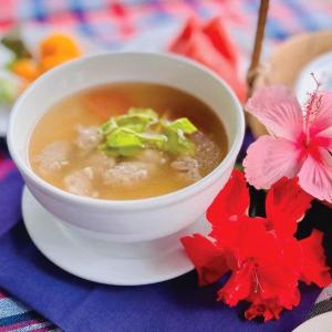 a bowl of soup on a plate next to flowers at Chababaancham Resort in Amphawa