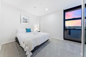 a white bedroom with a bed and a large window at Modern 2BR Free parking near Olympic park in Sydney