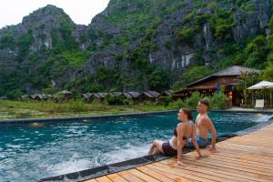 a man and woman sitting on the edge of a pool at Karsia Retreat Ninh Binh in Ninh Binh