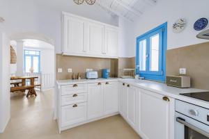 a kitchen with white cabinets and a blue window at Maison Mariel in Skopelos Town