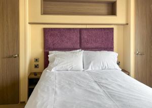 a bedroom with a white bed with a purple headboard at Whitehouse Holiday Park in Abergele