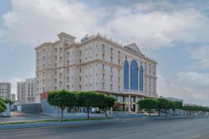 a large white building with blue windows on a street at Warwick Al Baha Hotel in Baljurashi