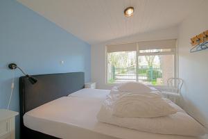 a bedroom with a bed with white sheets and a window at Vakantiehuis Duynloper - Julianadorp aan Zee in Julianadorp