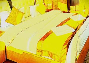 a large bed with yellow and white sheets and pillows at The Trisha Hotel in kolkata