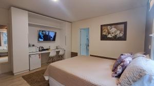 a bedroom with a bed and a desk and a kitchen at Hospedagem Jardins de Gramado in Gramado