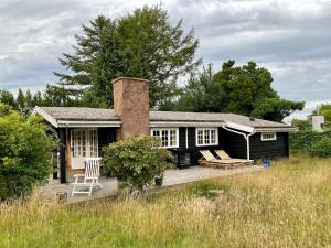 a black house with a brick chimney and a deck at Cozy and authentic log house in Dronningmølle
