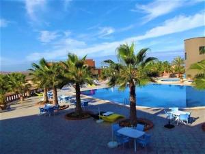 a resort with a pool with palm trees and chairs at L'Echappée Belle in Sidi Boû el Fedâïl