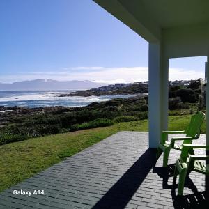 a porch with green chairs and a view of the ocean at ROMANZA APARTMeNT in De Kelders