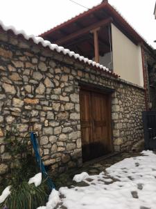 a stone house with a wooden door in the snow at Ξενώνας Το Πάλαι Ποτέ in Polydrossos