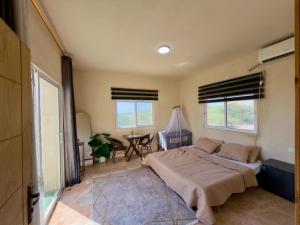 a bedroom with a bed and a table and two windows at Entire Home Near Deadsea & Baptism Site Pool, Garden, BBQ, Great Price in Shūnat Nimrīn +13 photos