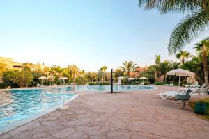 a swimming pool with chairs and umbrellas in a resort at Atlas Golf Resort in Marrakesh