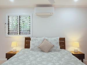 a bedroom with a bed with two lamps and a window at Private Rainforest Cottage - Bingil Bay in Mission Beach