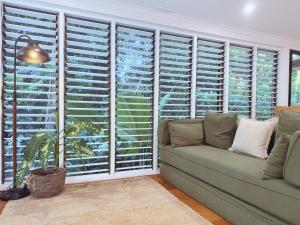 a living room with a couch and a window with shutters at Private Rainforest Cottage - Bingil Bay in Mission Beach