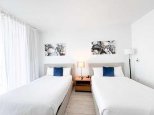 two beds in a room with white walls and blue pillows at 30th Fl Beachwalk Studio Bay Balcony in Hallandale Beach