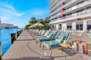 a row of chaise lounge chairs next to the water at 30th Fl Beachwalk Studio Bay Balcony in Hallandale Beach +50 photos